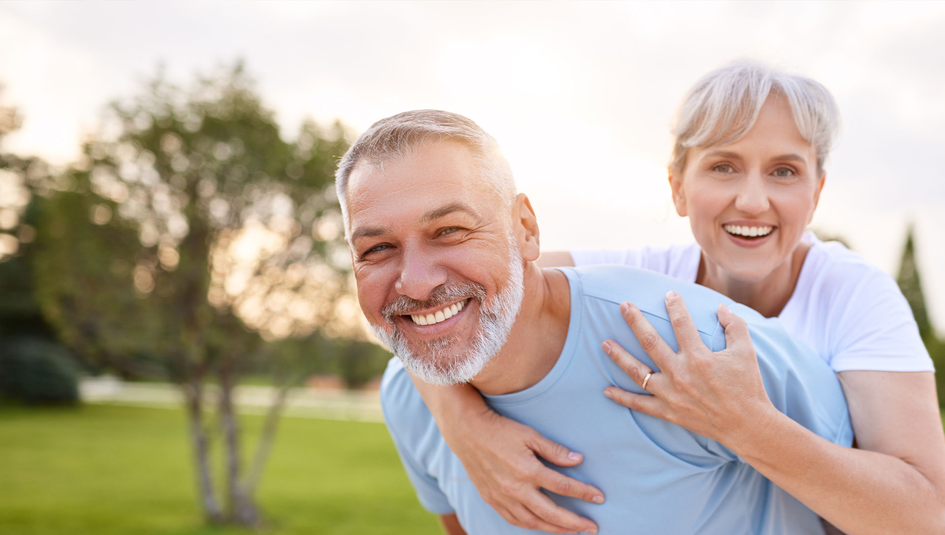 An elderly couple embracing and smiling, enjoying a sunset moment in a park.