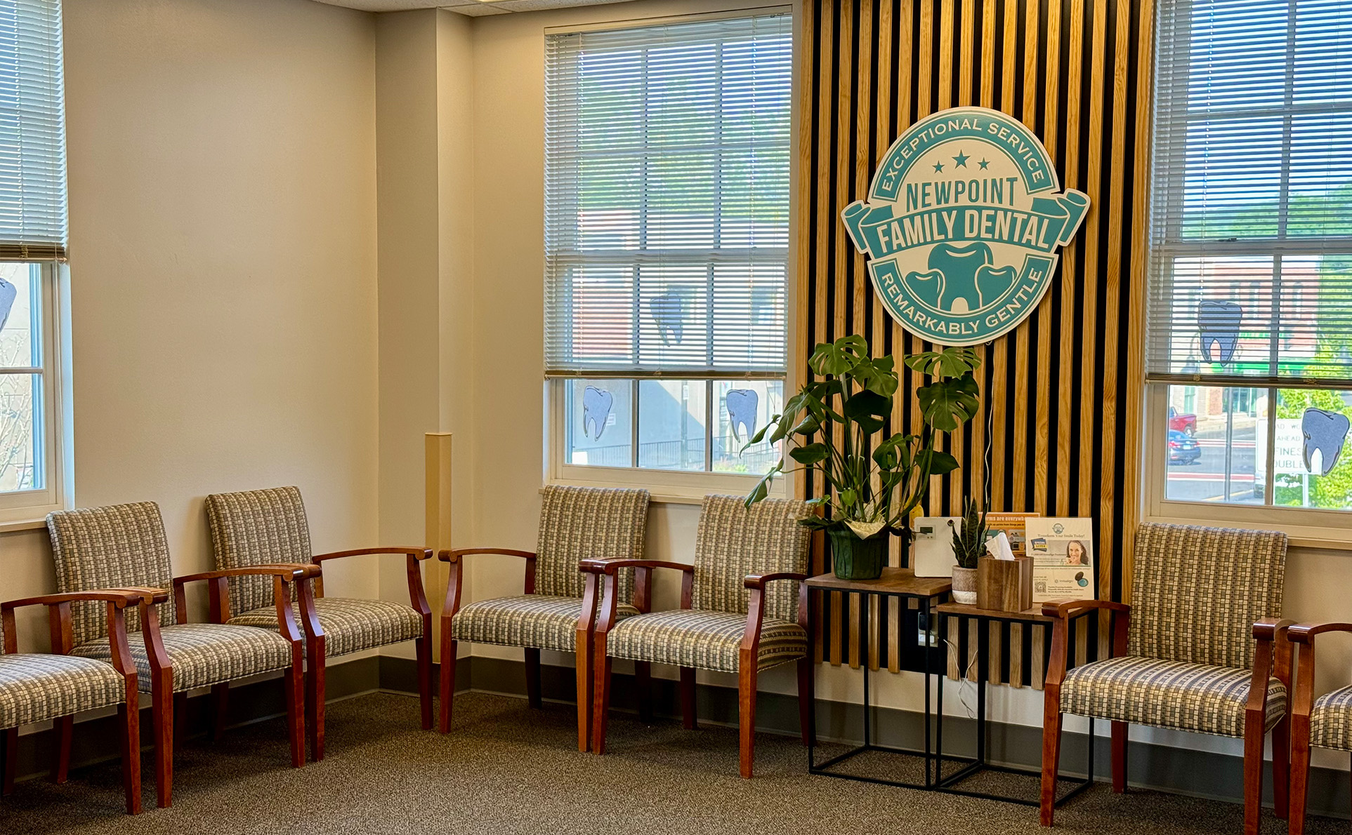 The image shows an interior space with a sign that reads Naperville Downtown and features furniture including chairs and a couch, along with decorative elements such as framed pictures and a potted plant.