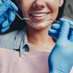 A woman sitting in a dental chair, smiling at the camera, with a dentist performing a procedure on her teeth.